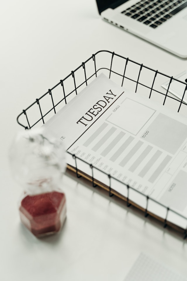 Hourglass beside a wire basket containing weekly planner pages.