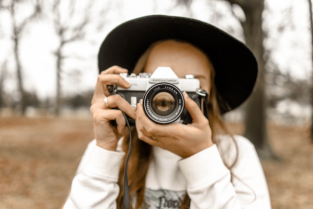 Femme portant un chapeau noir utilisant un appareil photo pour prendre une photo.