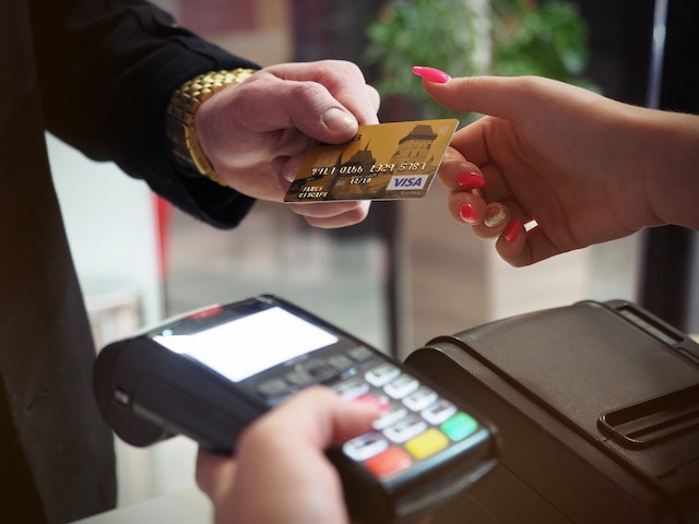 A customer and cashier handing each other a credit card over a black payment terminal