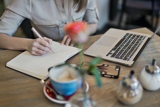 Persoană care scrie pe un notebook lângă Macbook.