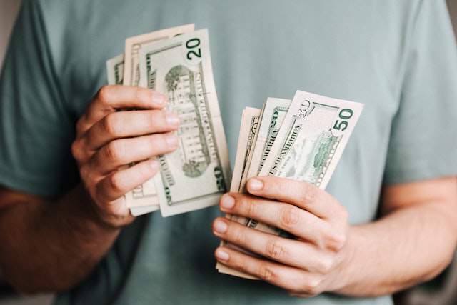 Man with an unseen face holding and counting US banknotes.