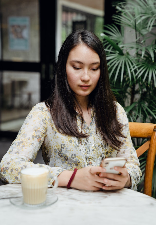 Femeie asiatică care trimite mesaje pe telefonul mobil într-o cafenea stradală