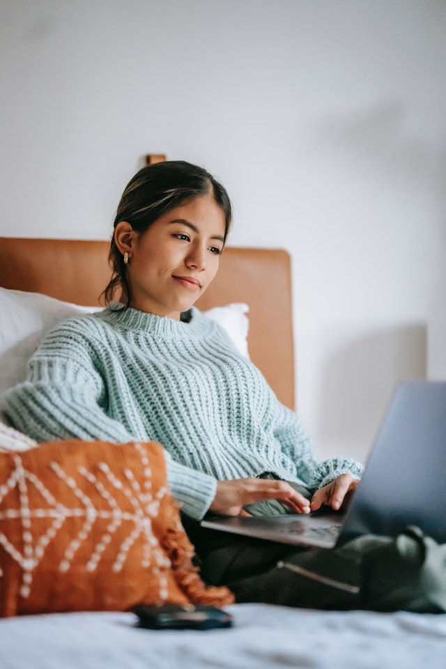 Junge Frau arbeitet freiberuflich mit einem Laptop auf dem Bett.