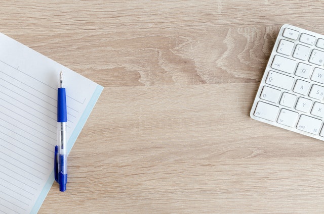 Blue Retractable Pen on Top of Notebook Near Magic Keyboard.