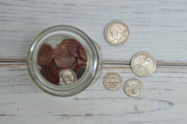 Coins inside a glass jar and on a painted wooden table.