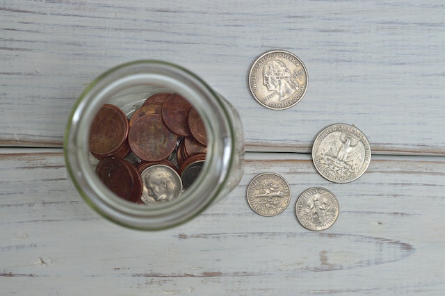 Moedas dentro de um frasco de vidro e sobre uma mesa de madeira pintada.