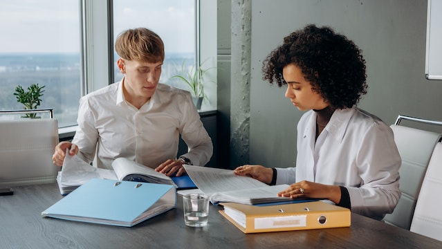 Colleagues in white long-sleeve shirts sitting and reading a financial report in a conference room.