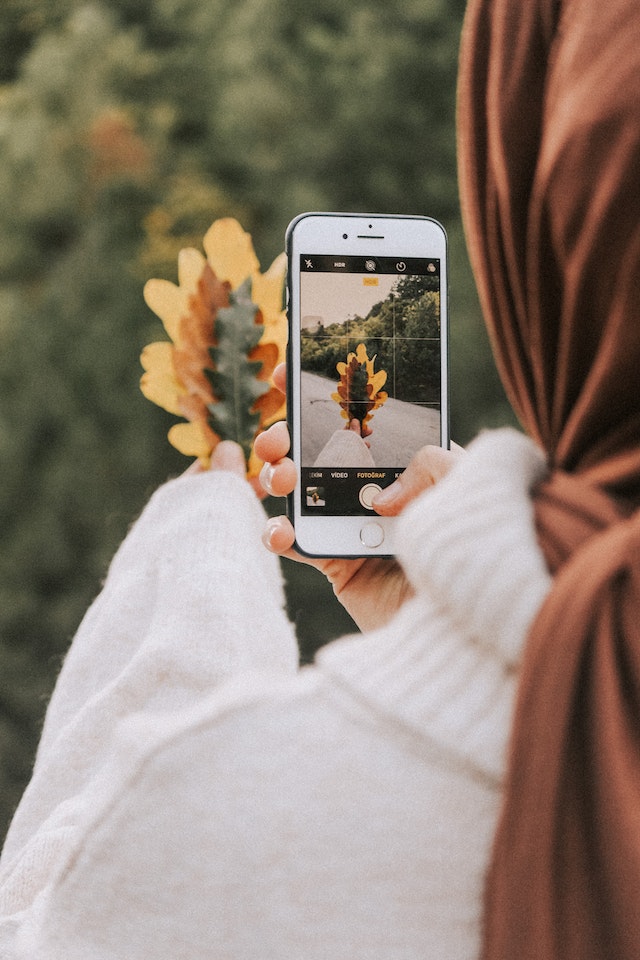 Femeie luând o fotografie de frunze uscate