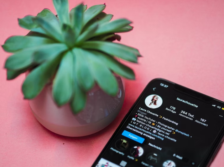 Un iPhone nero con l'account Instagram di un influencer su una superficie rosa. 