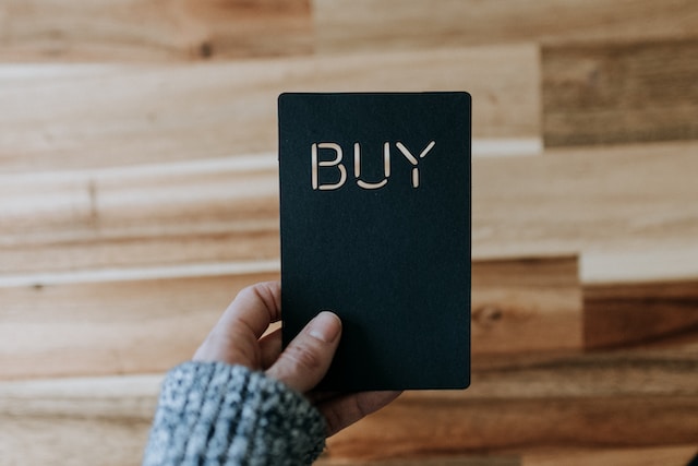 A woman holding a black card with the word “BUY” on it.