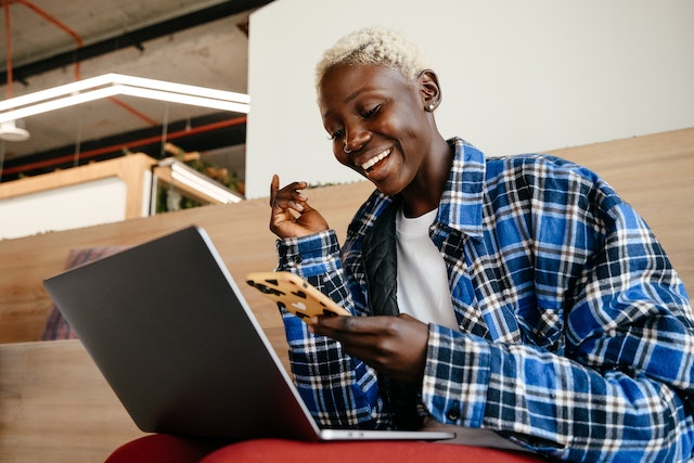 An influencer smiling happily at her phone as her Instagram followers increase.