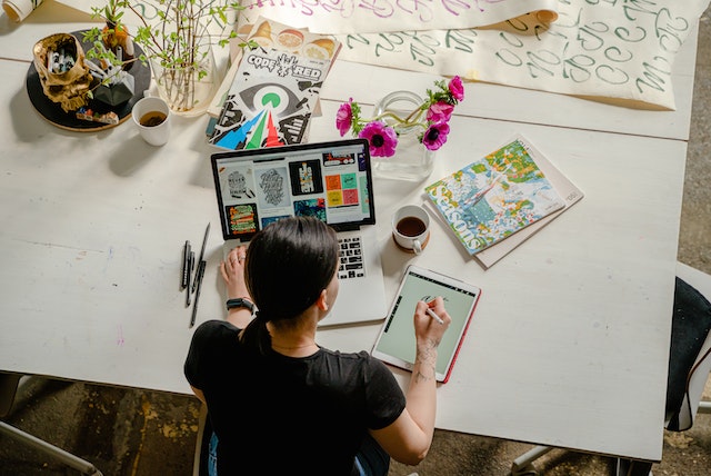 Woman writing quotes on her tablet while using a laptop for inspiration.