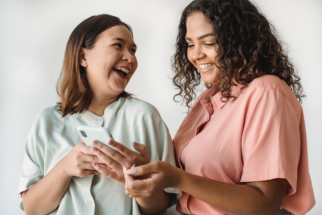 Duas mulheres a olhar para um telemóvel e a sorrir uma para a outra.