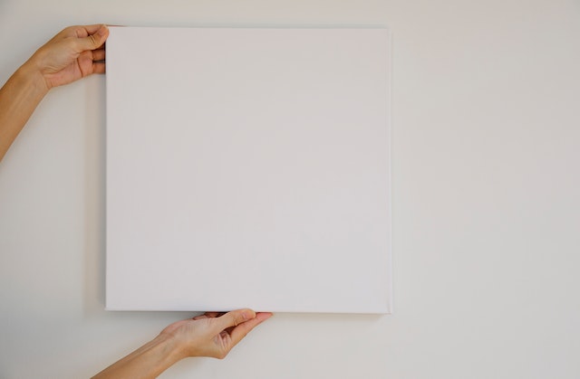 Unseen person holding a blank canvas up to a wall.