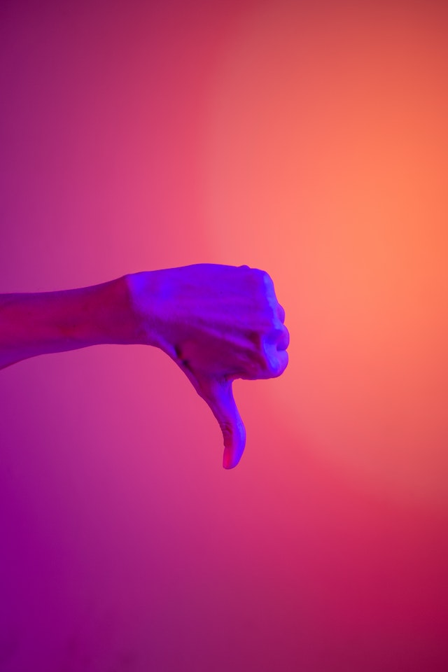 Unseen person performing a thumbs down among purple, orange, and pink lighting.