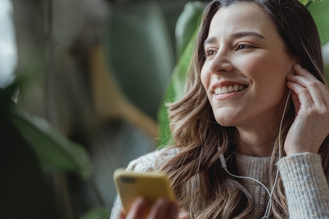 Mujer con auriculares y sosteniendo su teléfono mientras sonríe y escucha música compartida en Instagram.