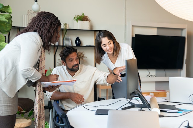 A man showing something on his monitor to his coworkers.