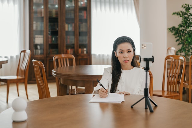 O femeie influencer stă în fața camerei de filmat, luând notițe de la publicul său live.