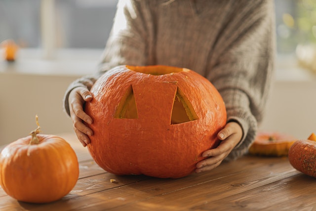 Frau schnitzt ihre Jack O' Lantern für ihr Herbst-Halloween Instagram post.