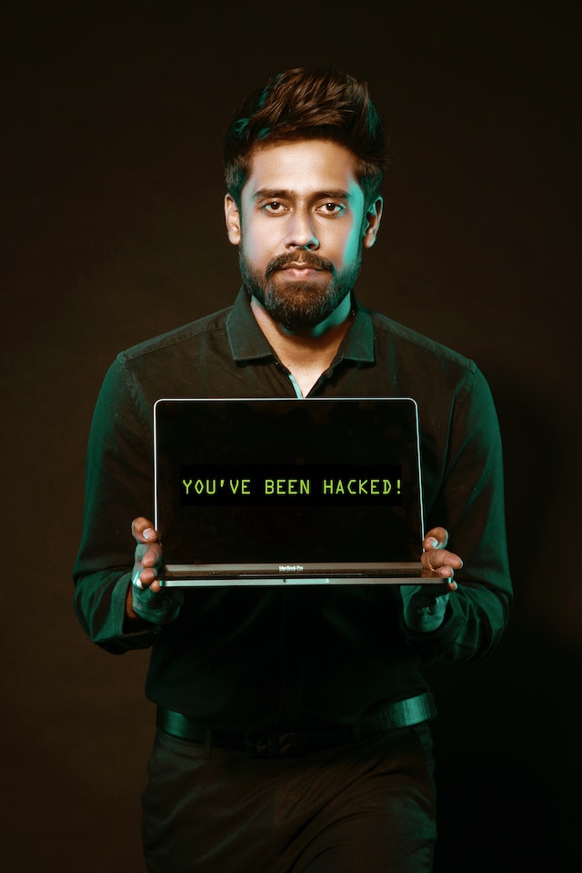 Man holding a laptop with both hands with a message on the screen saying “You’ve been hacked.”