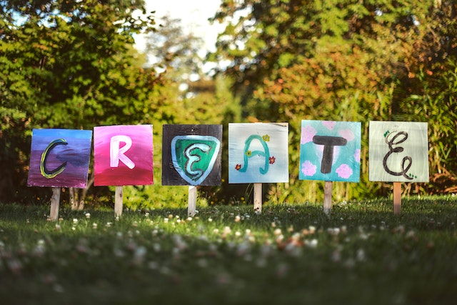 Painted sign staked into flowering grass, reading “Create.”