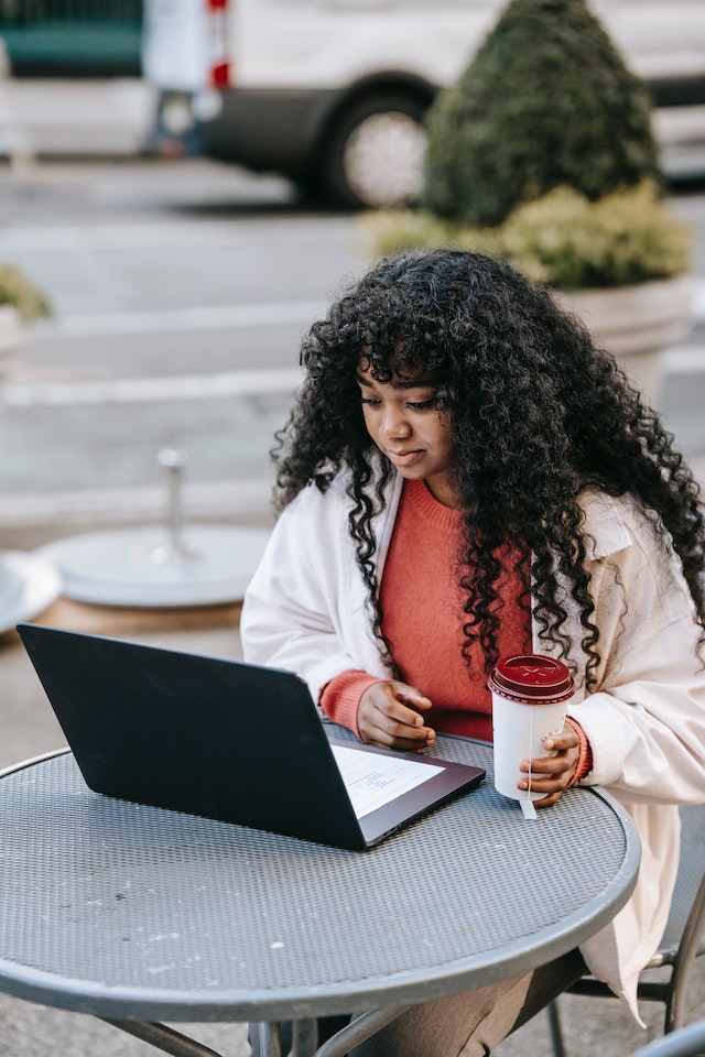 Woman using a laptop while having a beverage in a street cafe.