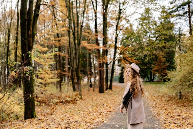  Frau, die in einem Park spazieren geht, der von vielen Bäumen mit Herbstlaub gesäumt ist.