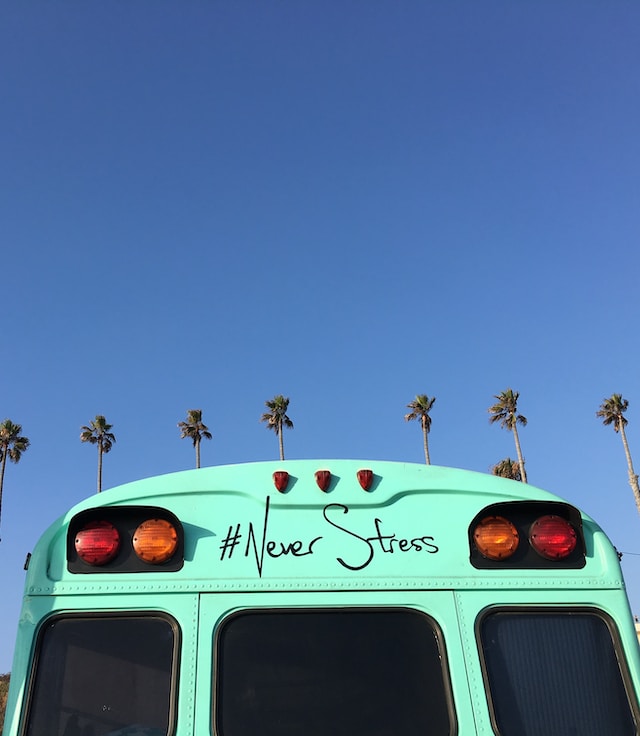 Image of a turquoise bus with the painted phrase “#Never Stress” next to palm trees.