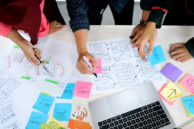 Three individuals writing on paper and sticky notes