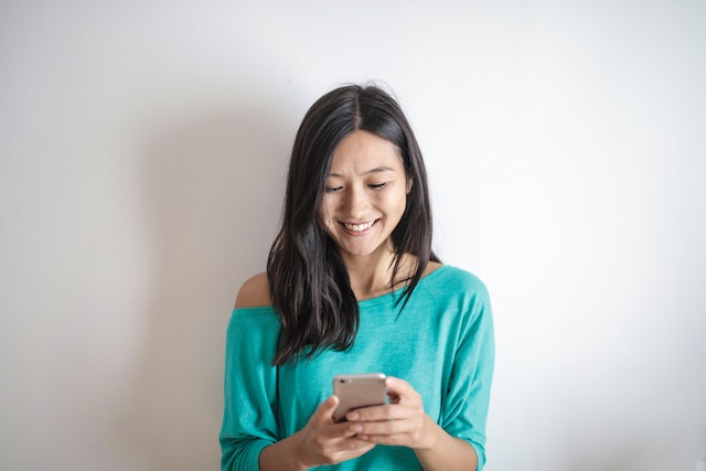 A woman wearing a teal shirt smiles as she replies to messages on Instagram.
