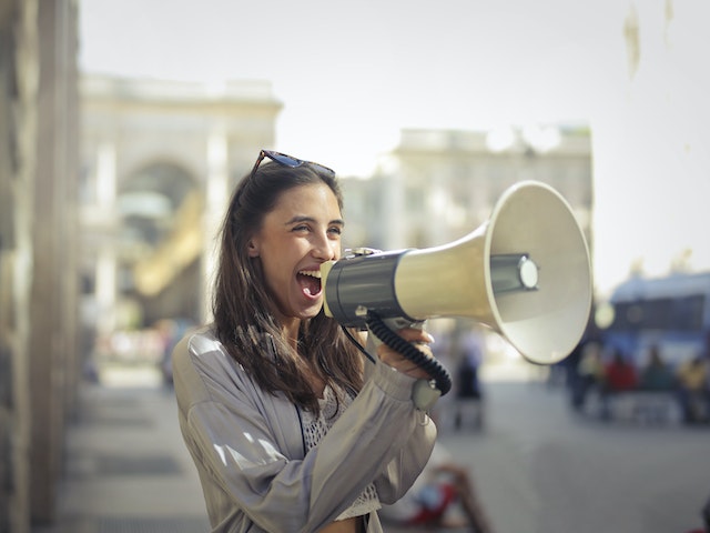 Uma mulher alegre grita num megafone para despertar o interesse.