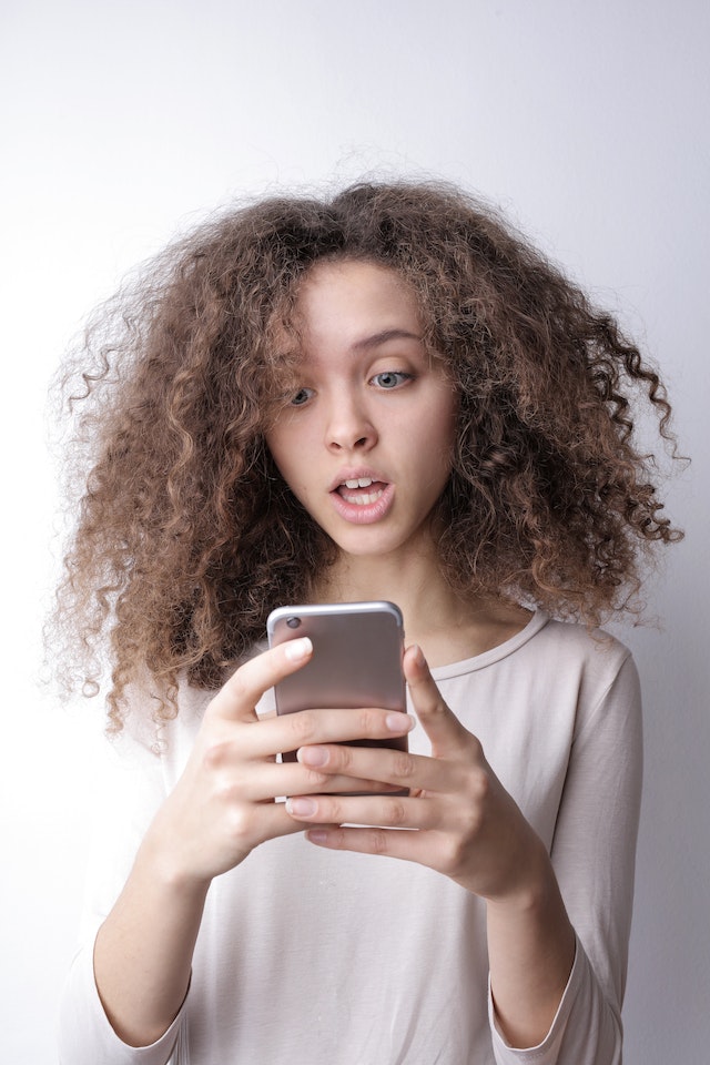Instagram 、未読メッセージの多さに驚きながら携帯電話を手にする若い女性。
