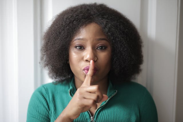 A woman holds her index finger over her mouth to indicate she’s telling a secrety.