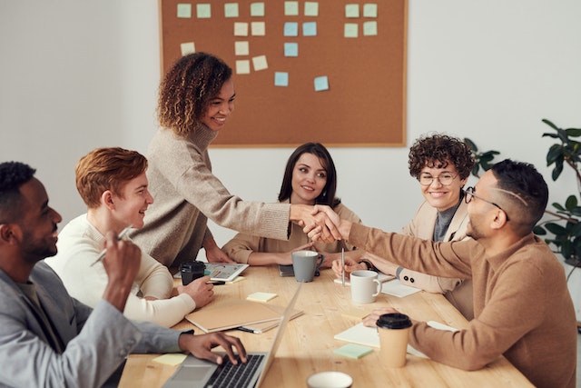 Eine Markeninhaberin schüttelt dem Marketingteam, das sie gerade für ihr Unternehmen eingestellt hat, die Hand.