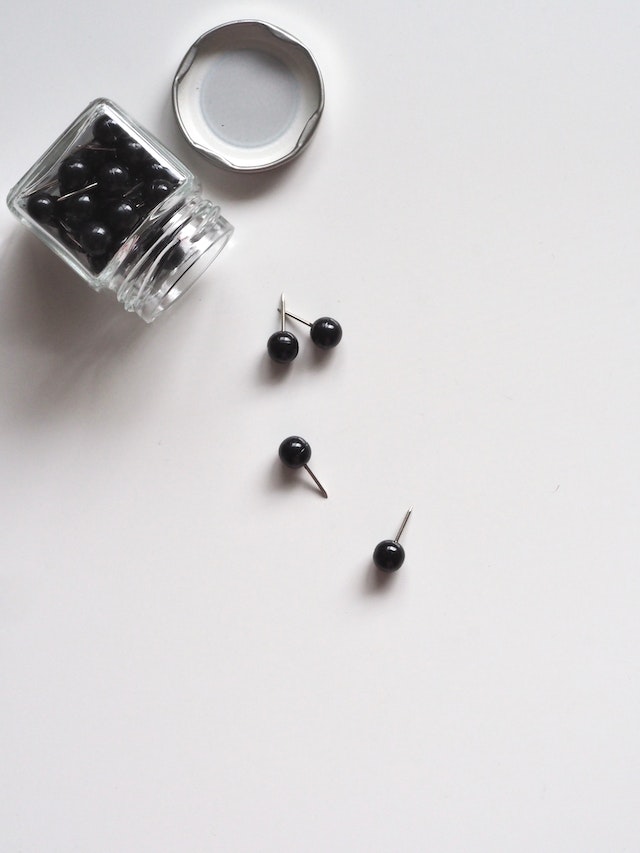 Chinchetas negras que caen de un pequeño tarro de cristal con la tapa abierta.
