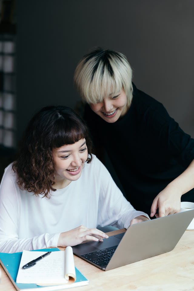 Doi prieteni care folosesc împreună un laptop într-o cameră.