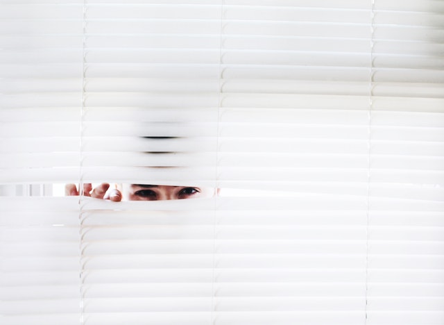 A Person secretly peeking through window blinds.