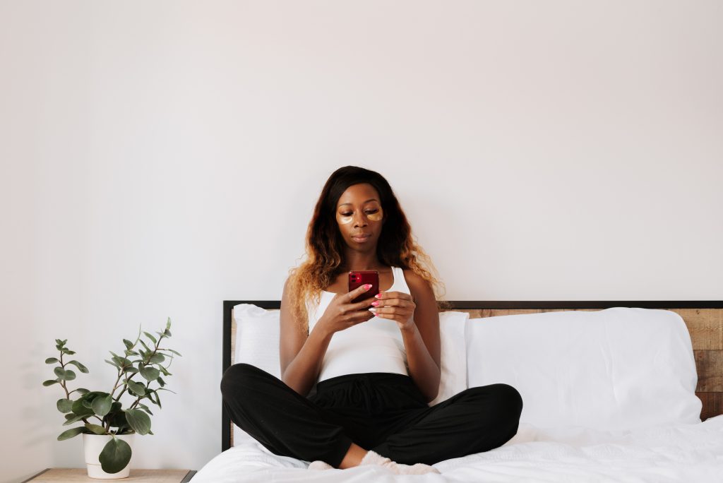 An influencer wearing eye patches and sitting in bed, edits her reels to gain more followers and increase engagement.