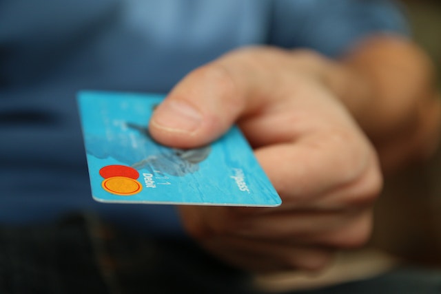 Unbekannte Person hält eine Debitkarte vor, um Kommentare online zu kaufen.