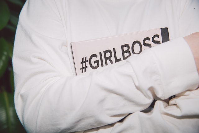 A woman is holding a book with a hashtag symbol and the phrase “girl boss” on it.