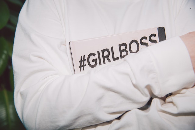 Una donna tiene in mano un libro con il simbolo di un hashtag e la frase "girl boss".