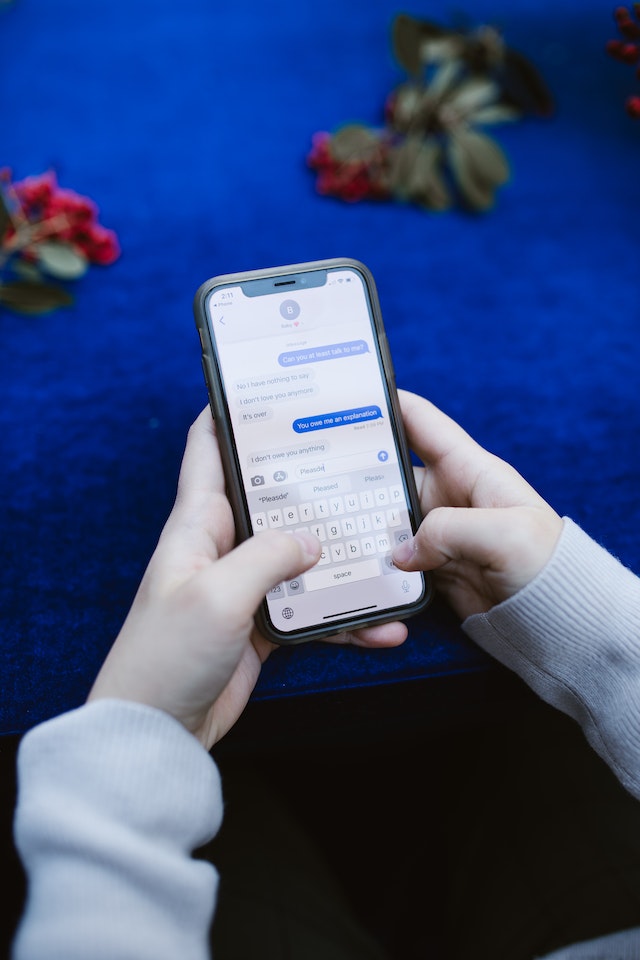 Un téléphone affiche une conversation textuelle entre deux personnes tandis qu'une personne assise à une table tape une réponse.