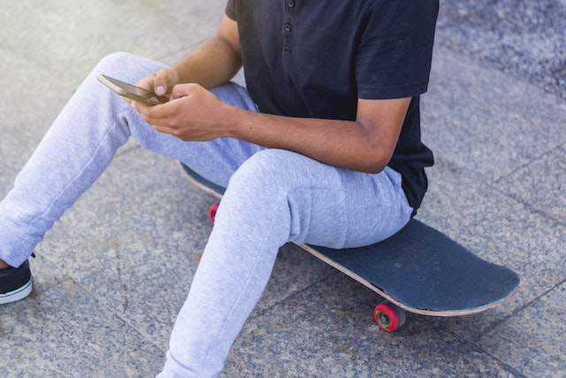 A person sits on a skateboard while trying to configure new hashtags. 