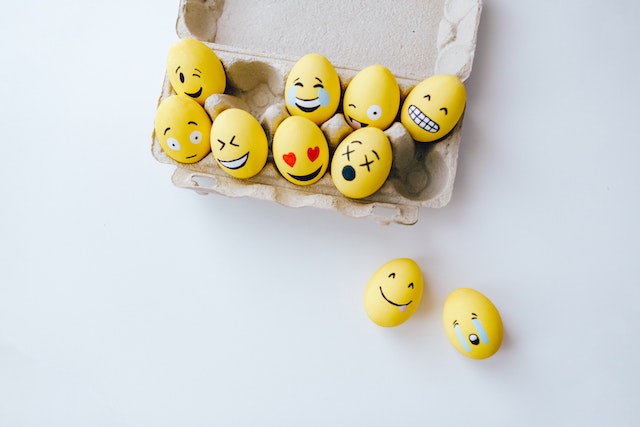 Facce emoji gialle dipinte su uova che cadono da un cartone di uova.