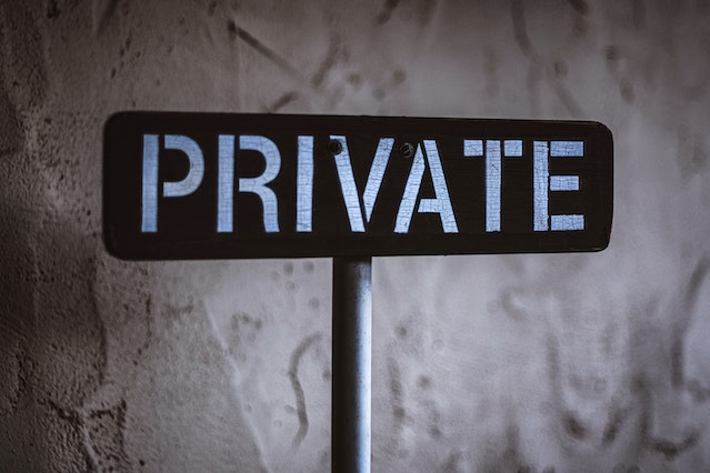 Een zwart-wit houten bord met de tekst "Private" voor een betonnen muur. 