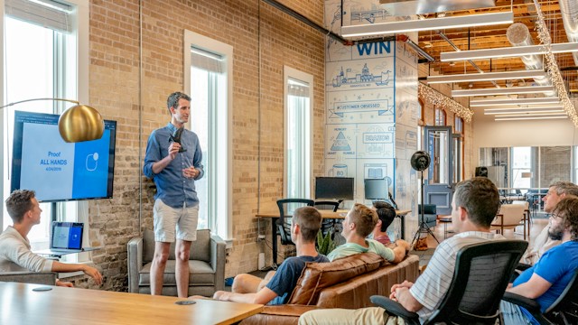 A group of people listening to one man in a blue shirt. 