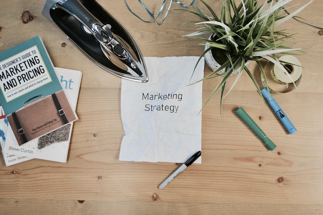 A picture of a paper with a "Marketing Strategy" print beside a plant vase, electric iron, and books.