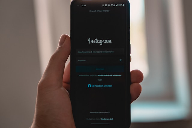 A picture of a hand holding a black smartphone displaying the Instagram app sign-in page.