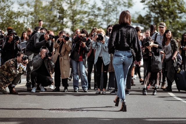 A celebrity walking down a road with paparazzi following her around.