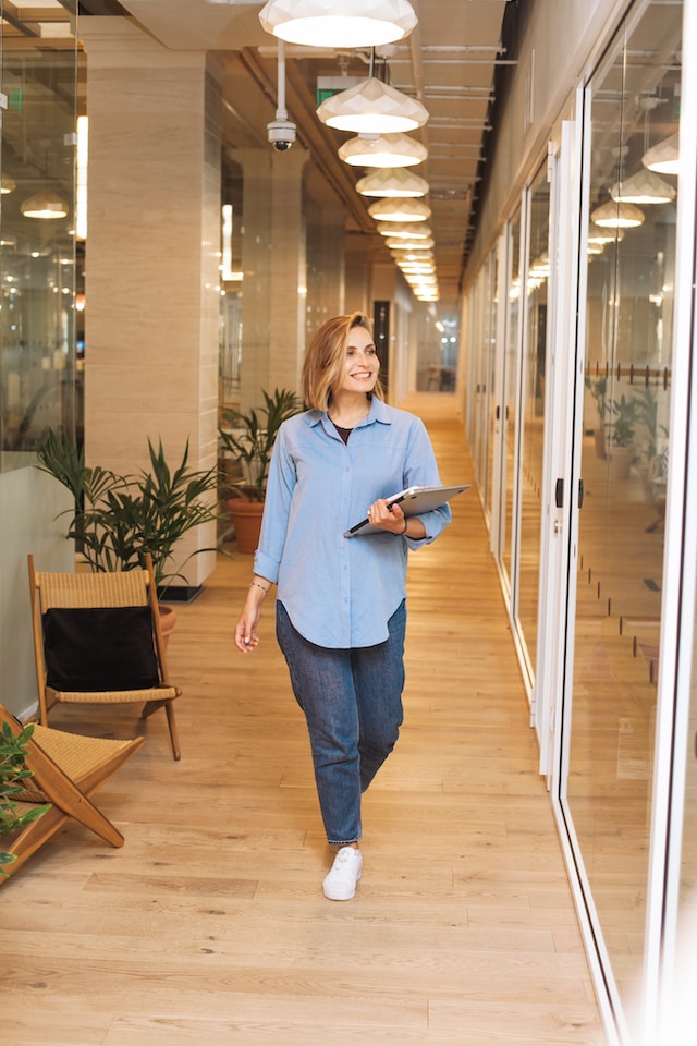 Une femme confiante en chemise bleue marchant avec un ordinateur portable.